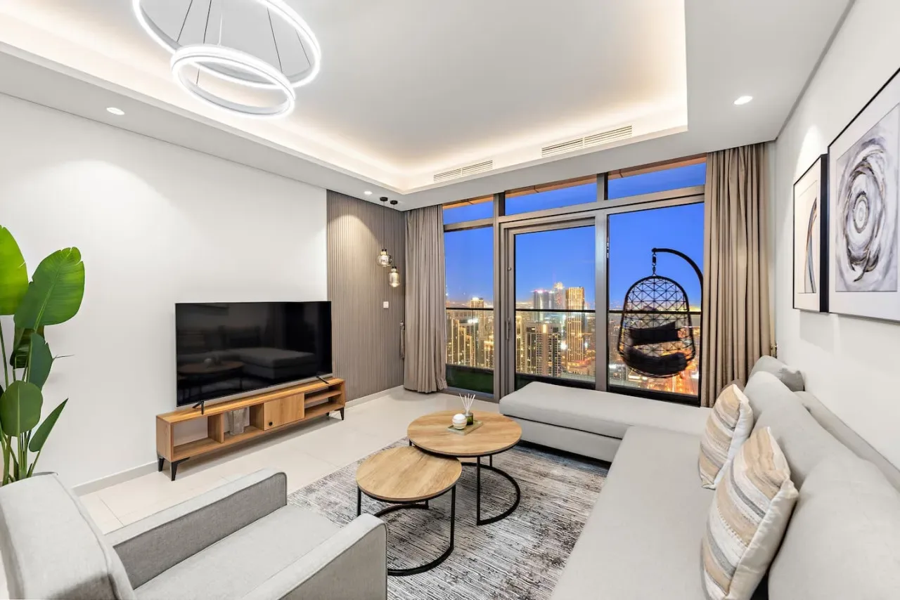 Una sala de estar moderna con grandes ventanas y vistas al horizonte urbano al anochecer.