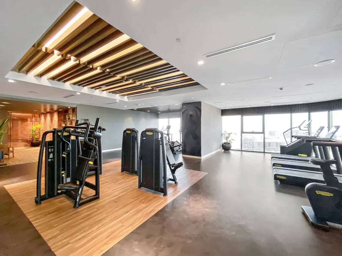 Un gimnasio con máquinas de ejercicio y cintas de correr junto a grandes ventanales.