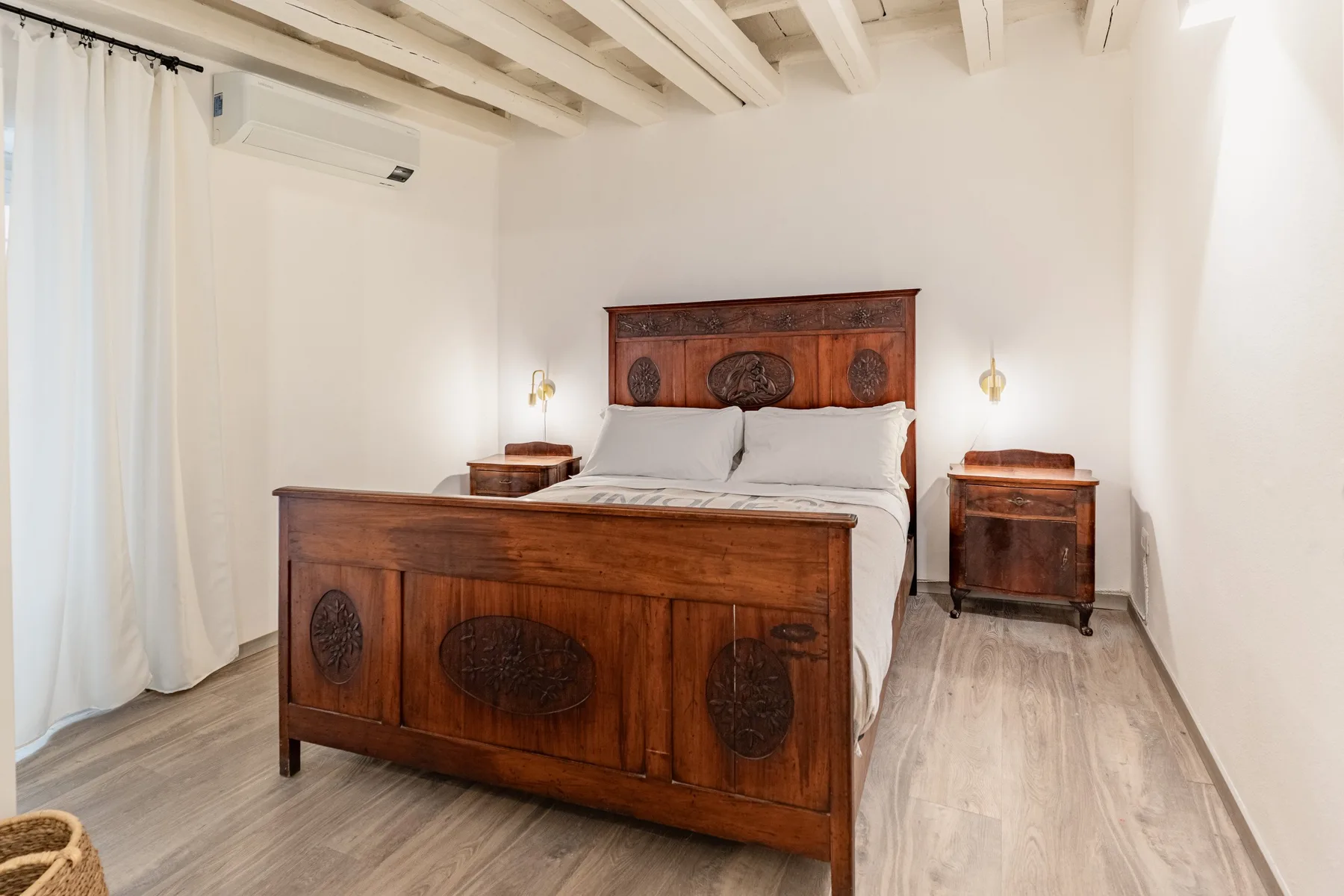 Dormitorio con una cama grande de madera, mesitas de noche y cortinas claras.