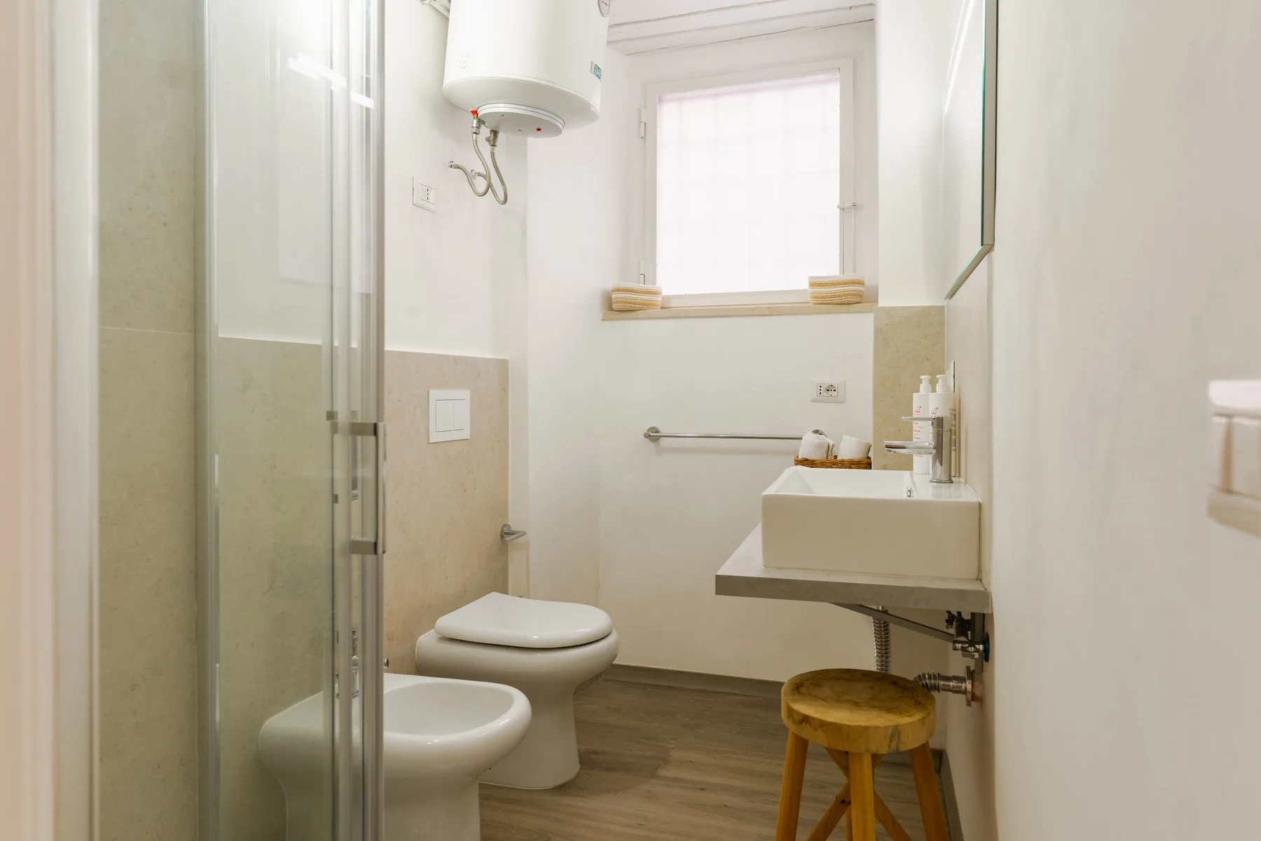 Un baño luminoso con ducha de vidrio, inodoro y lavabo suspendido.