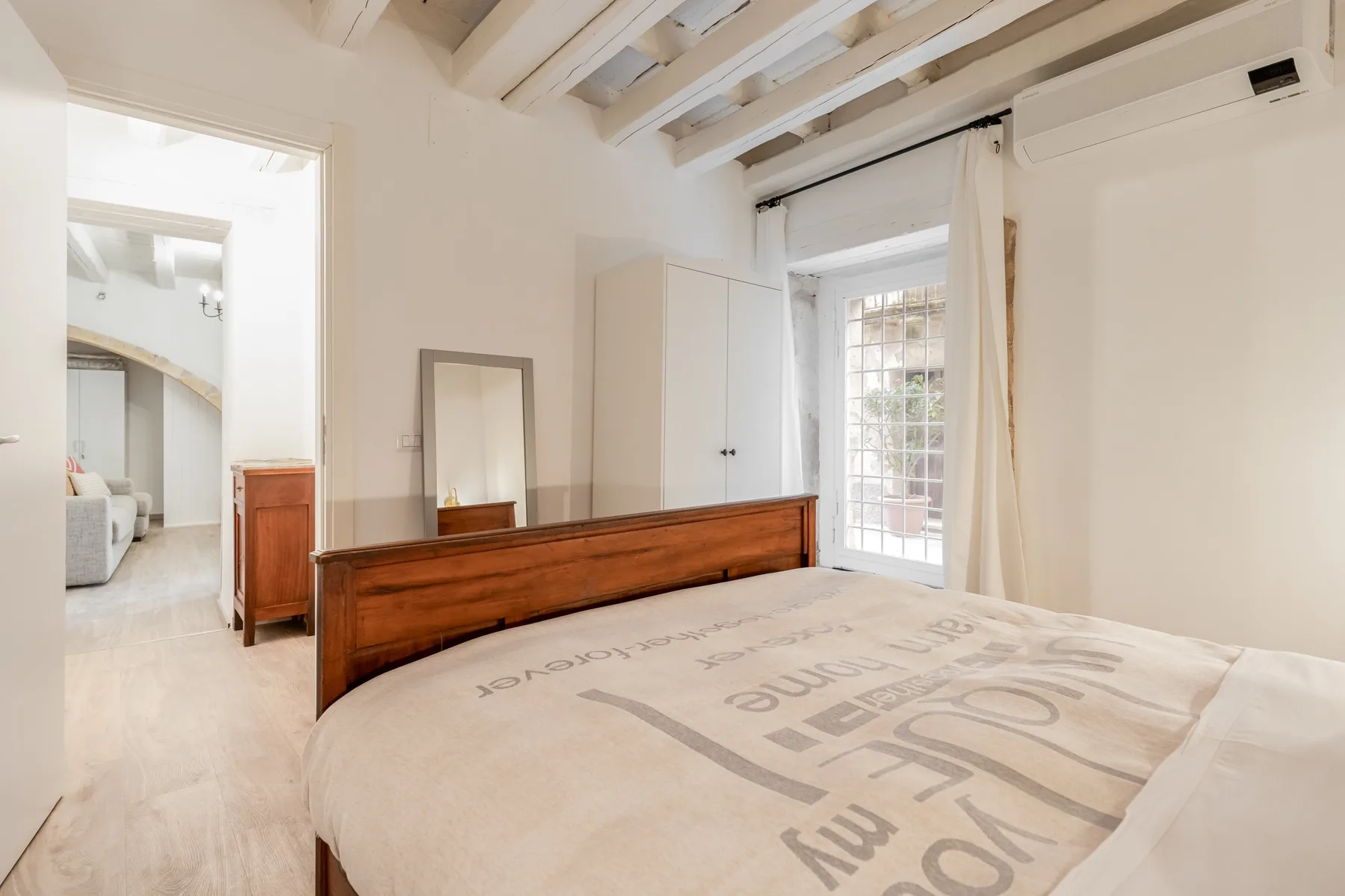 Un dormitorio luminoso con una cama de estructura de madera y una puerta acristalada.