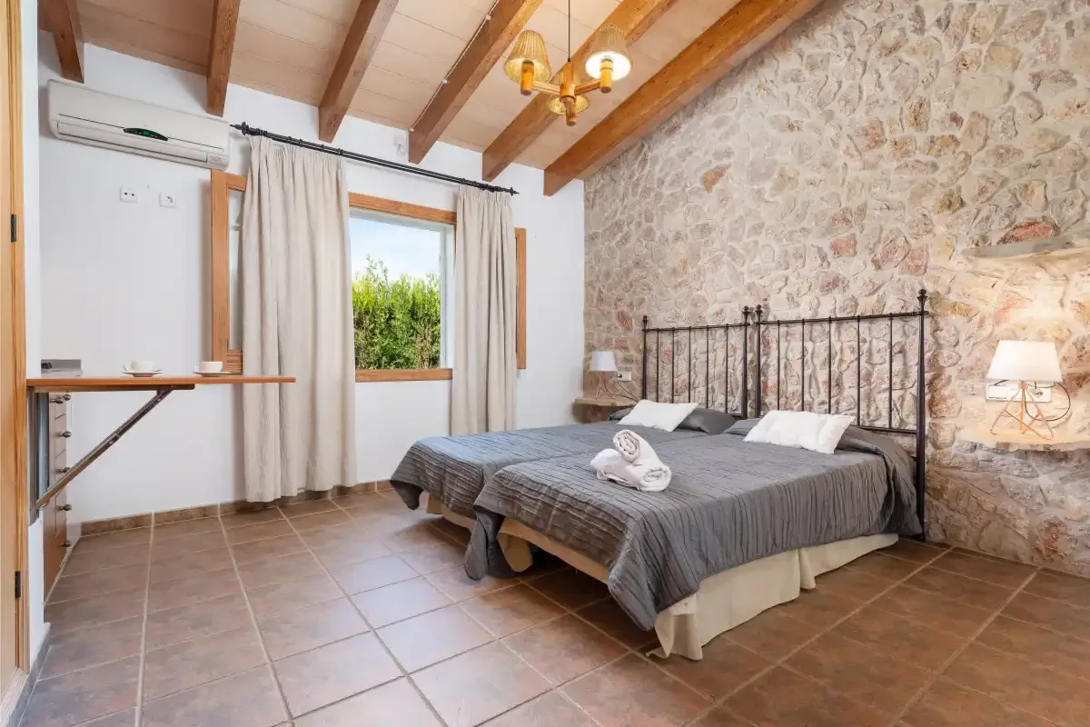 A bedroom with a bed against a stone wall and a curtained window.
