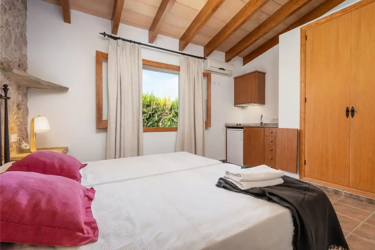 A bedroom with a bed, exposed wooden ceiling beams, and a window.