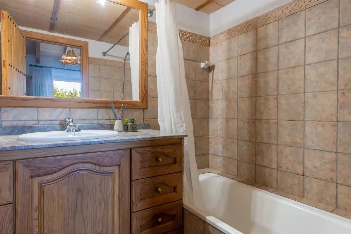 A tiled bathroom with a wooden vanity, sink, and bathtub.