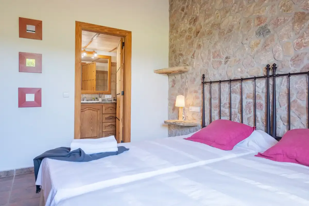 A bedroom with a bed, pink pillows, and a stone accent wall.