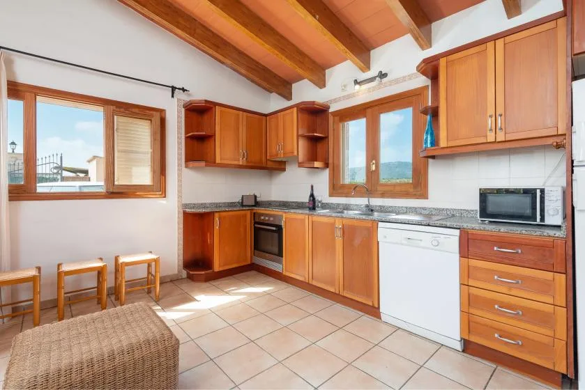 A bright kitchen with wooden cabinets, a tiled floor, and windows.