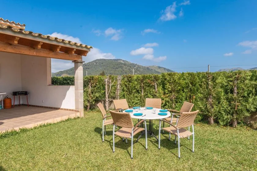 Outdoor dining area with a round table and seating beside a vine-covered fence.