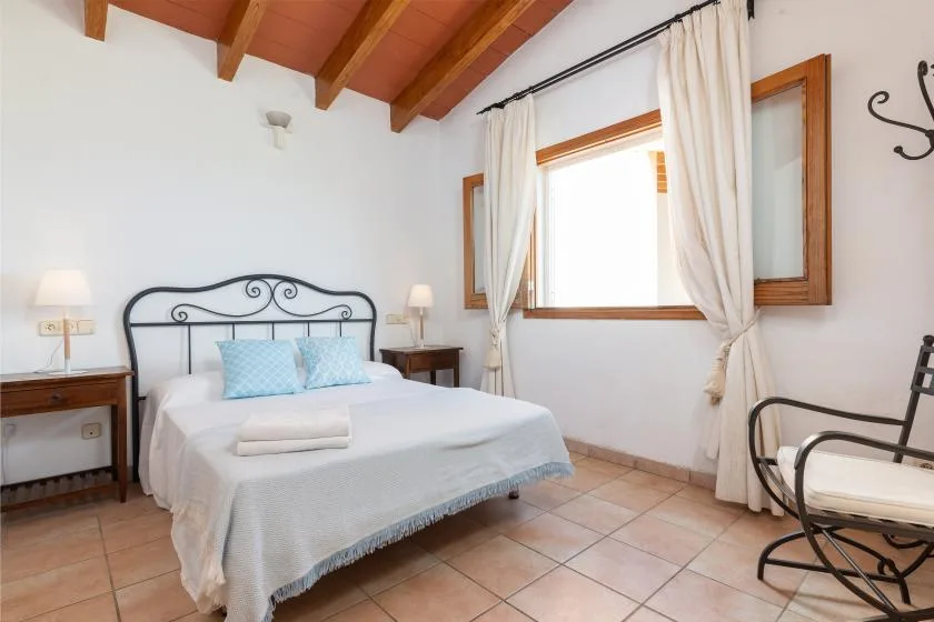 A bedroom with a bed, bedside tables, and a large window with curtains.