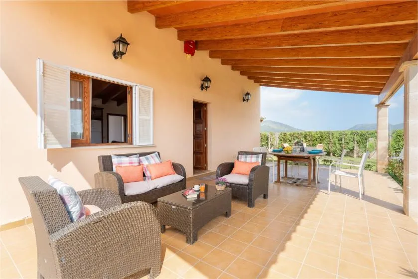 A covered outdoor seating area with wicker furniture and a table overlooking the landscape.