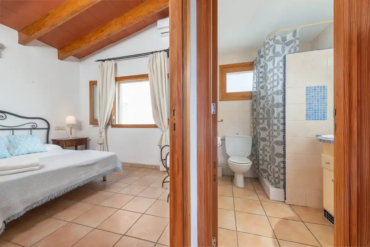 A bedroom with a bed and an adjoining bathroom with a shower and toilet.
