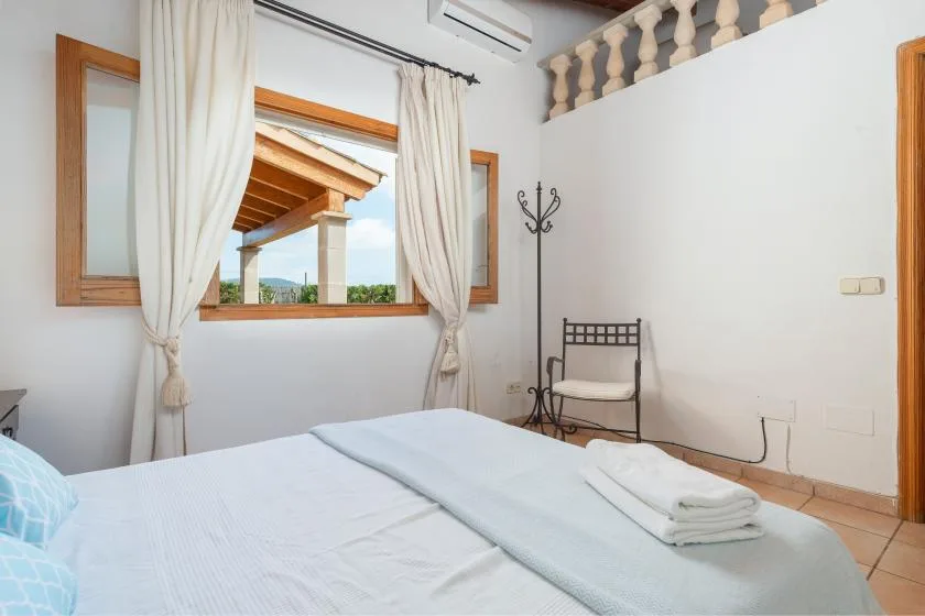 A bright bedroom with a bed beneath a curtained window.