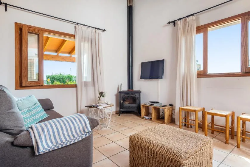 A bright living room with seating, a wood-burning stove, and windows overlooking greenery.