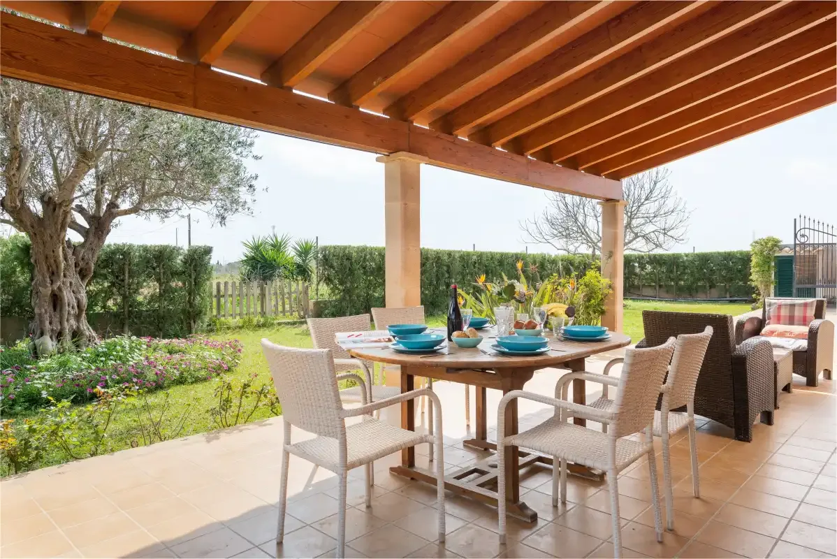 A covered outdoor dining area with a table and seating beside a garden.