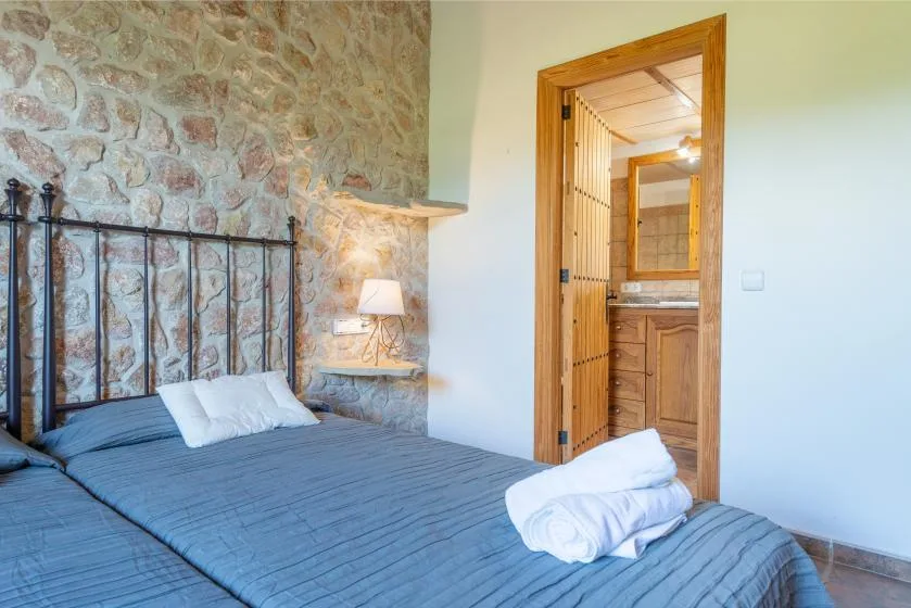 A bedroom with a blue-covered bed beside a stone wall and an open doorway.