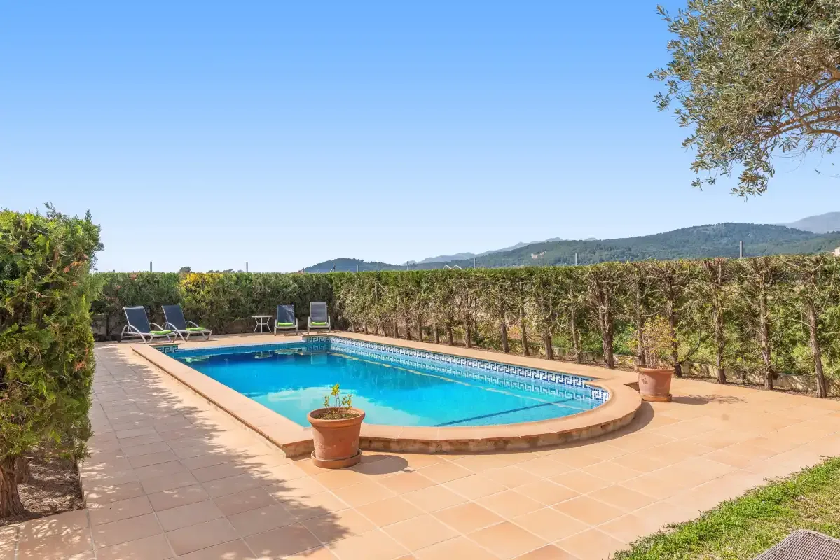 An outdoor swimming pool sits on a paved terrace beside clipped hedges.