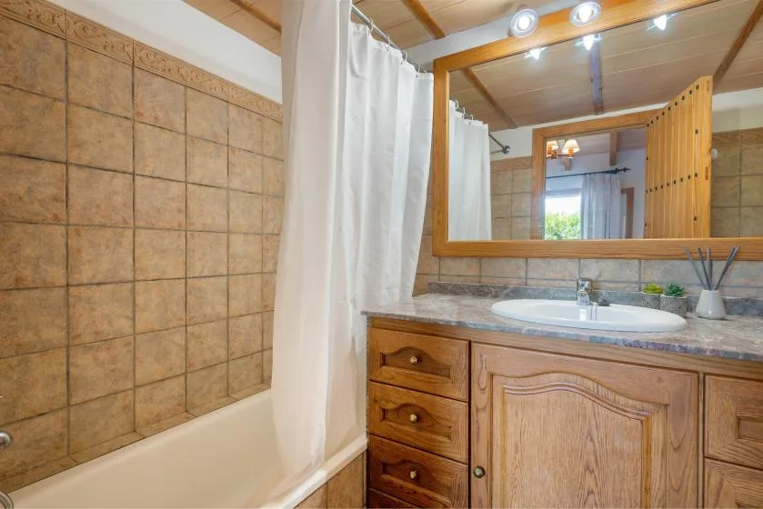 A bathroom with a bathtub, shower curtain, and wooden vanity.