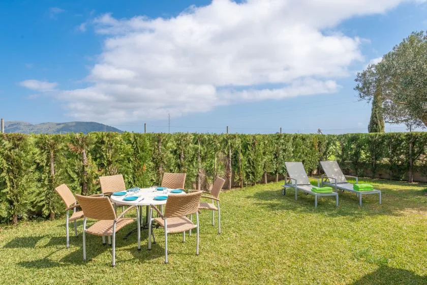 An outdoor garden seating area with a dining table and lounge chairs on the lawn.