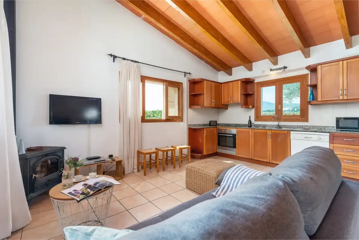 A living room opens onto a kitchen, with exposed wooden ceiling beams and a television.