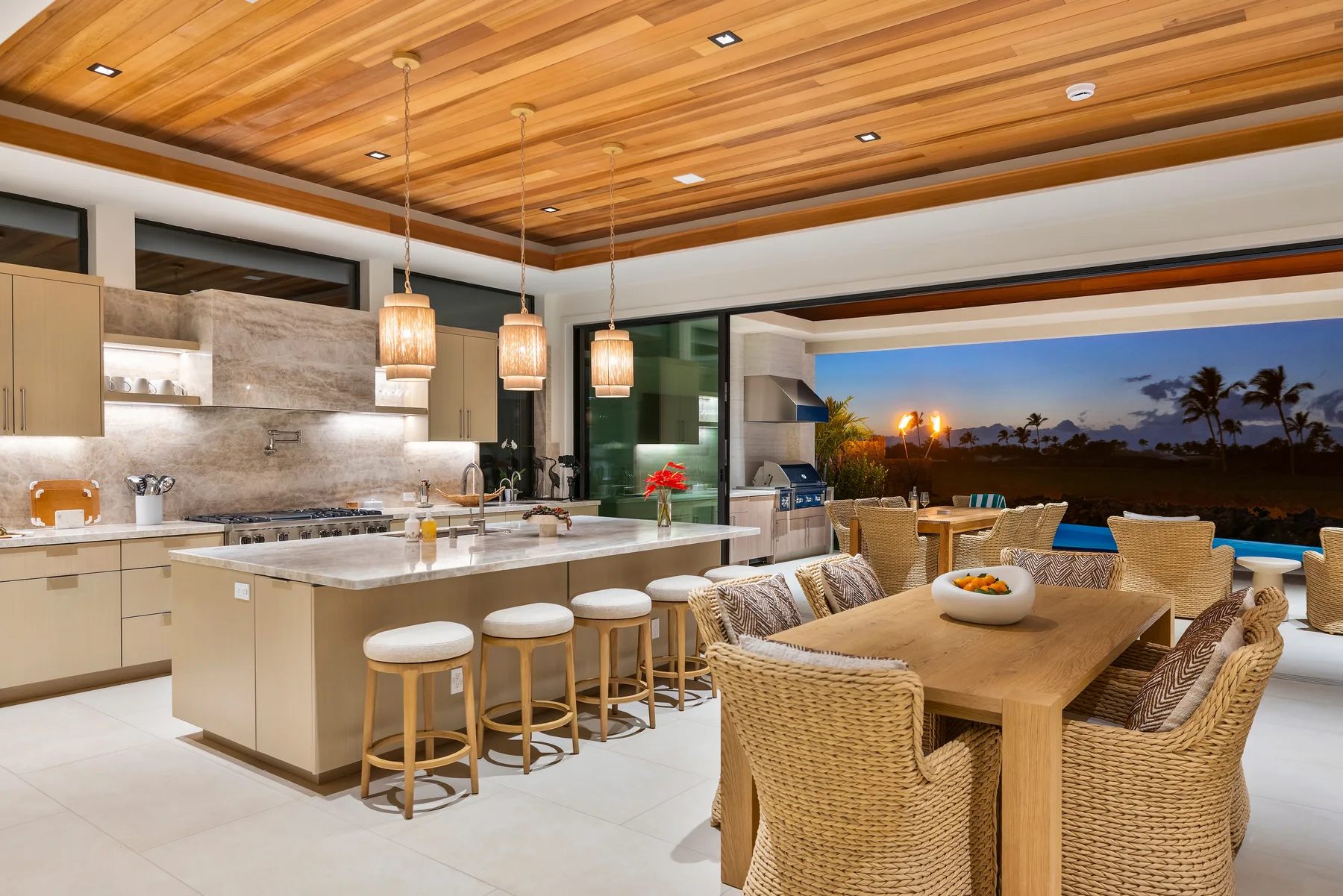 Una cocina abierta y comedor con una isla grande junto a una piscina al anochecer.