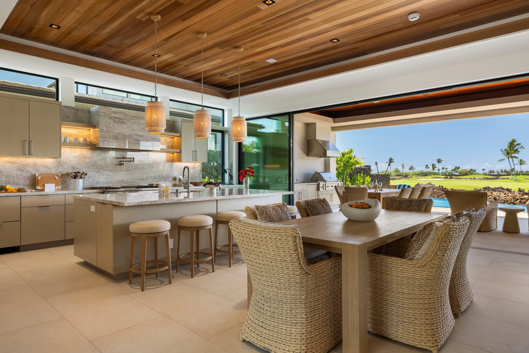 Una cocina abierta y zona de comedor con asientos de mimbre junto a un gran ventanal.