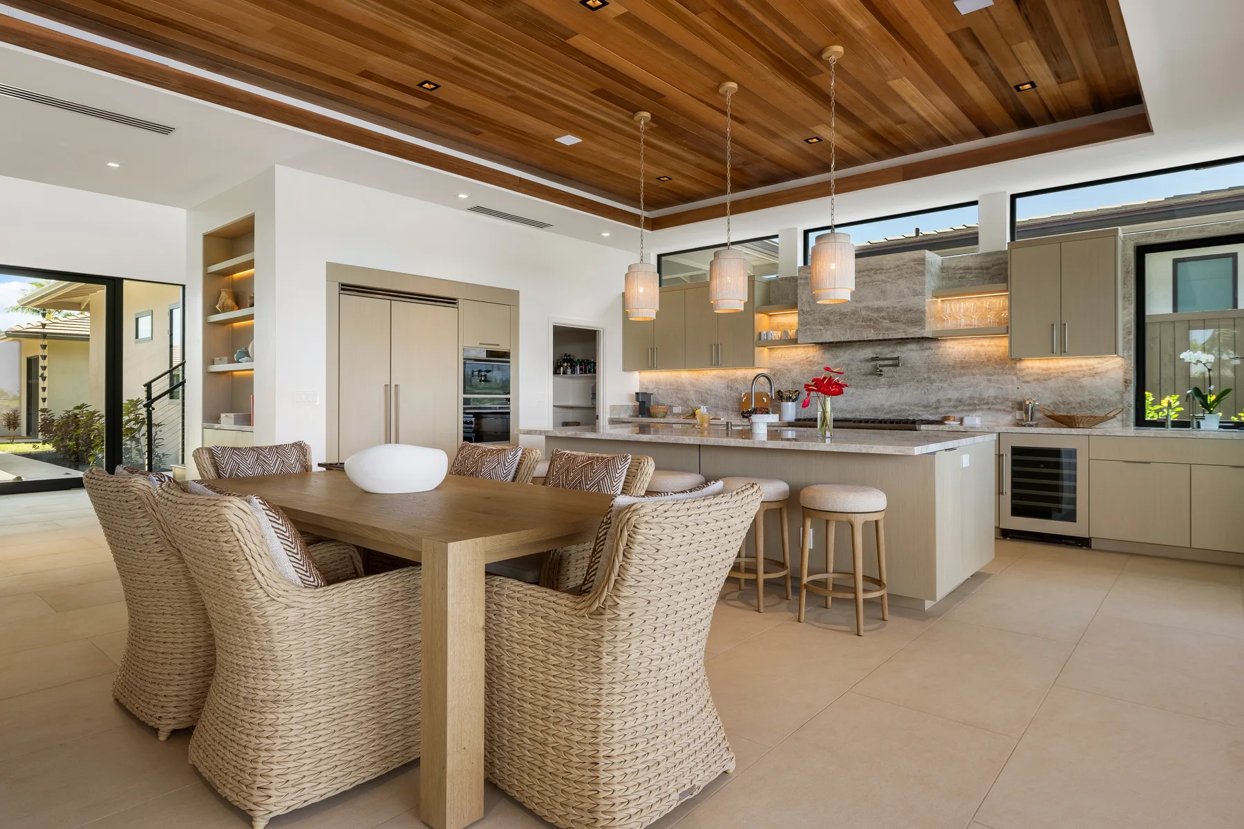 Un comedor abierto con cocina, mesa de madera y asientos tejidos.