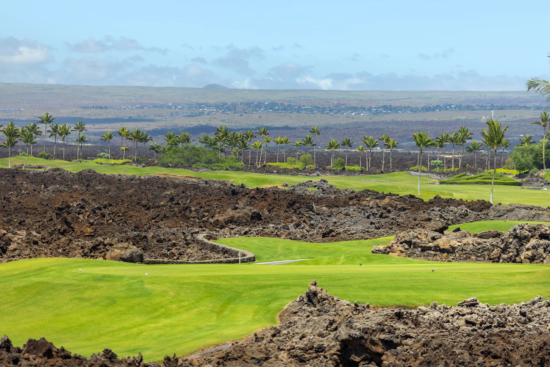 Un campo de golf con calles verdes bordeadas por roca volcánica oscura.
