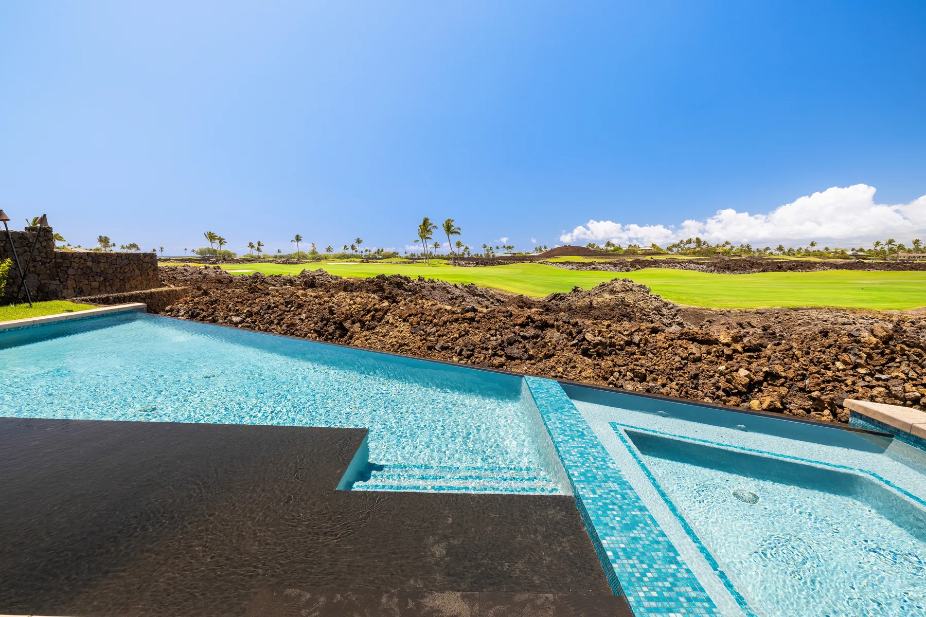 Una piscina bordea un paisaje rocoso y campos verdes.