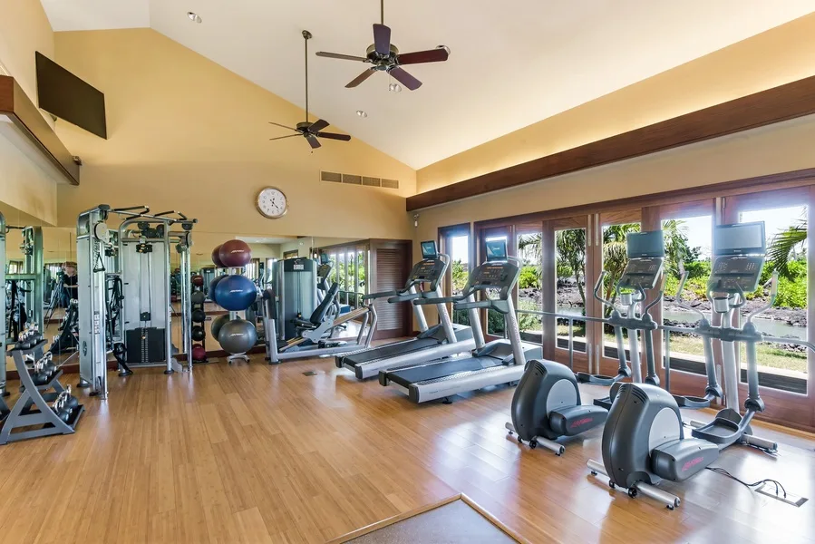 Una sala de ejercicio con máquinas y cintas de correr junto a grandes ventanas.