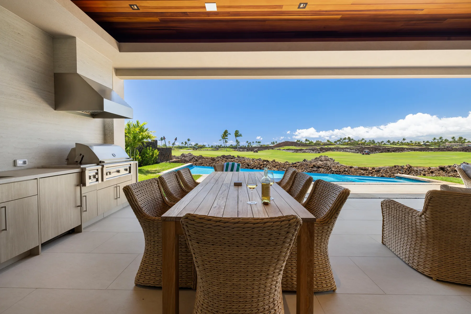 Un comedor al aire libre con asientos de mimbre da a una piscina y un paisaje verde.