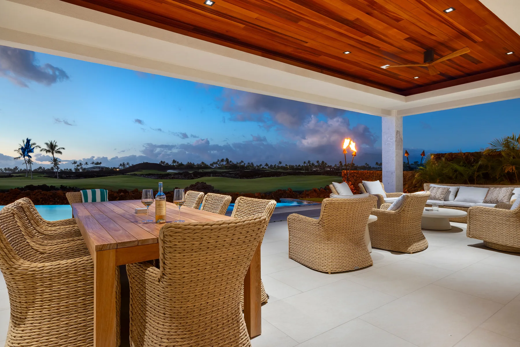 Una zona exterior cubierta de comedor y estar da a un paisaje al anochecer.