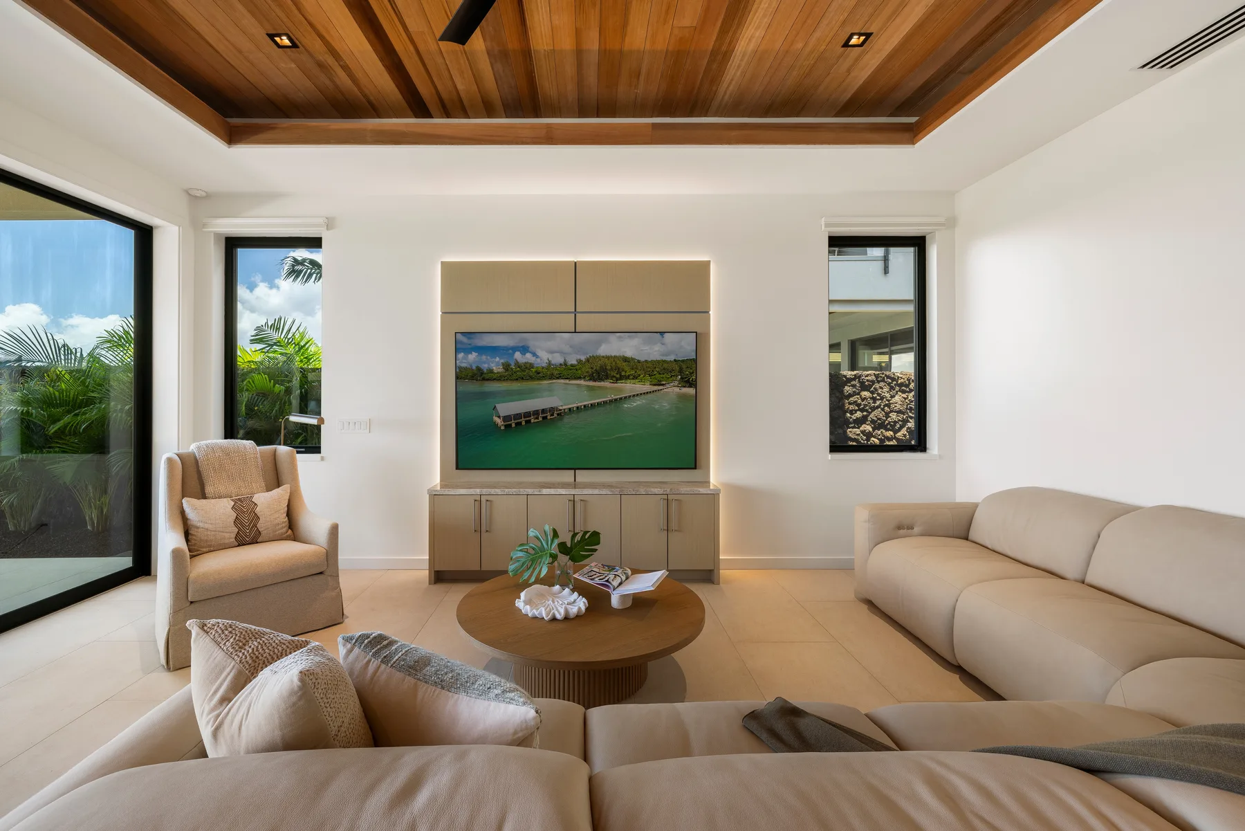 Sala de estar con asientos claros, una mesa de centro de madera y un televisor en la pared.