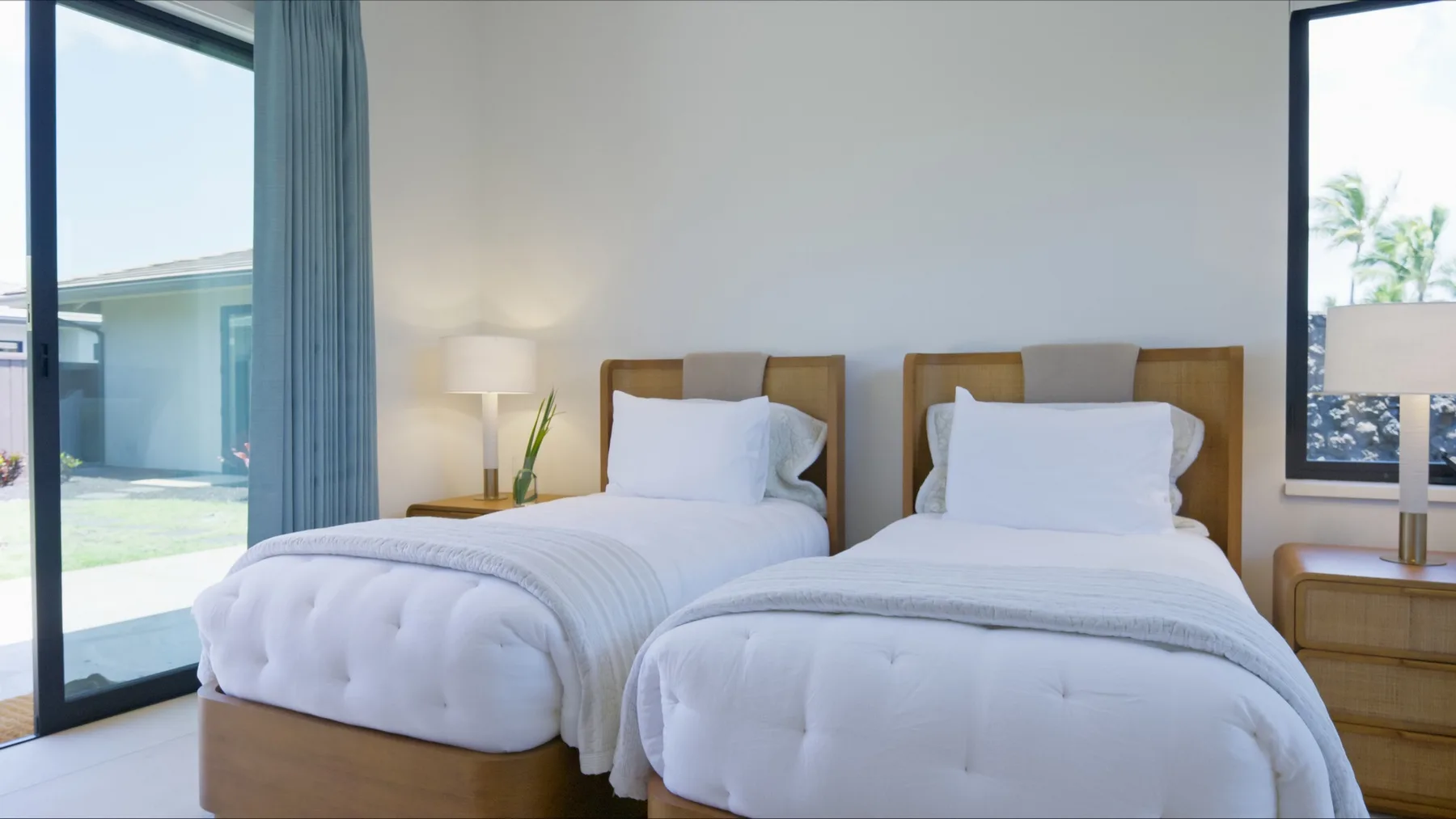 Un dormitorio luminoso con dos camas y grandes ventanales que dan a un jardín.