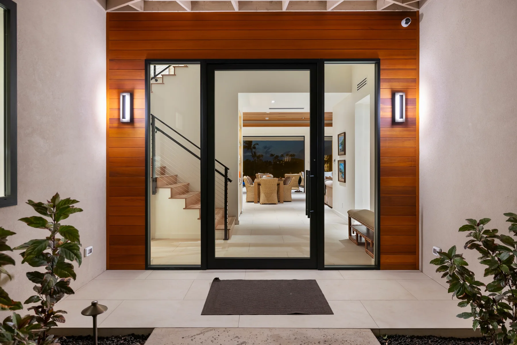 Una entrada moderna da a un interior luminoso con una escalera y una zona de asientos.