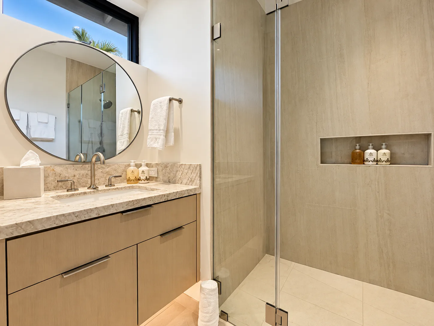 Un baño moderno con lavabo, espejo redondo y ducha de cristal.