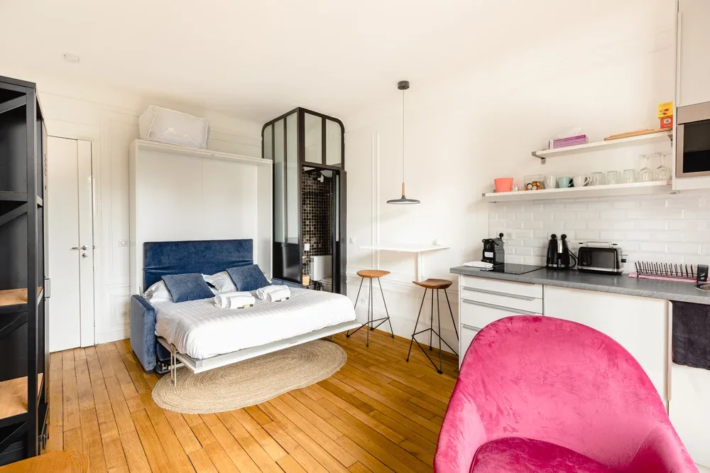 A bright studio room with a bed, a small dining area, and a kitchenette.