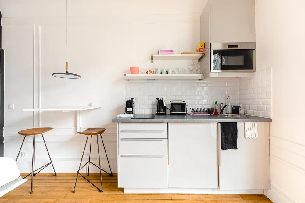 A bright kitchen with white cabinets, a counter, and a small dining table.