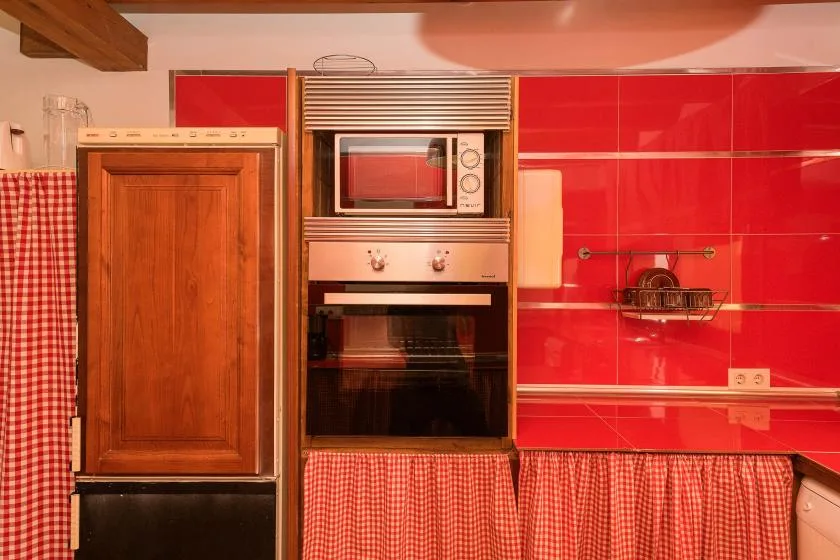 A kitchen with a built-in oven and microwave against a red tiled wall.