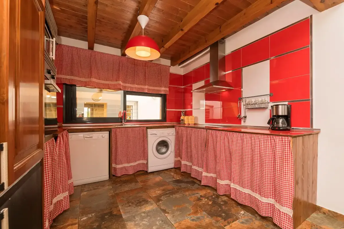A kitchen with red cabinetry, a patterned fabric skirt, and a washing machine.