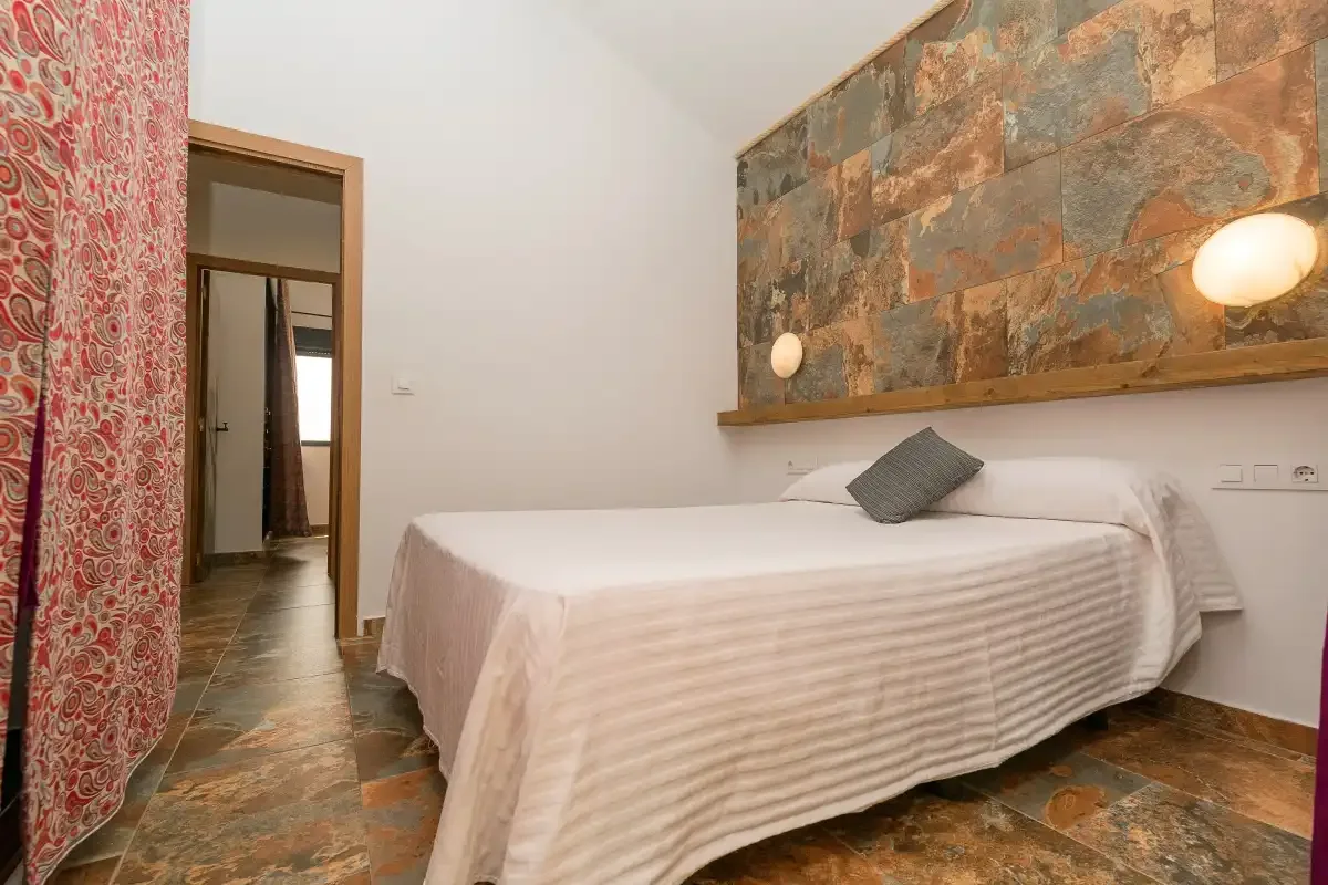 A bedroom with a neatly made bed and a patterned stone wall.
