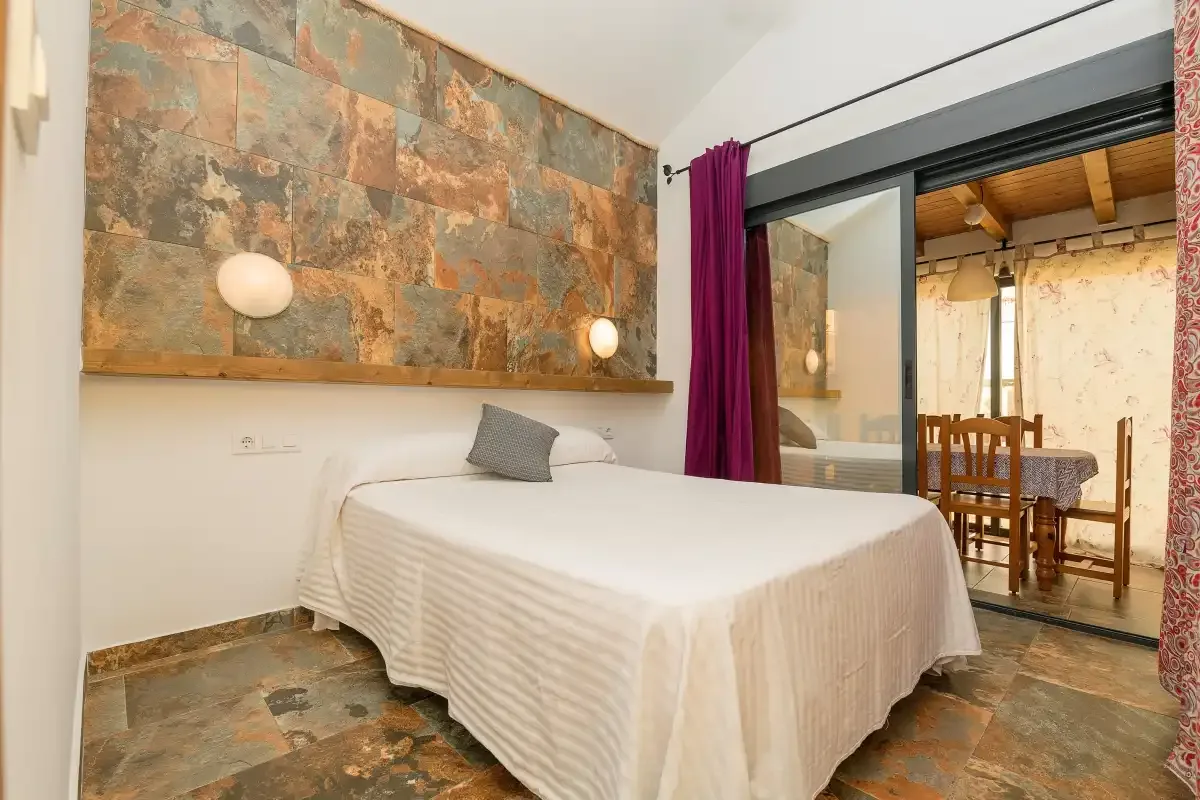 A bedroom with a bed beside a glass partition overlooking a dining area.