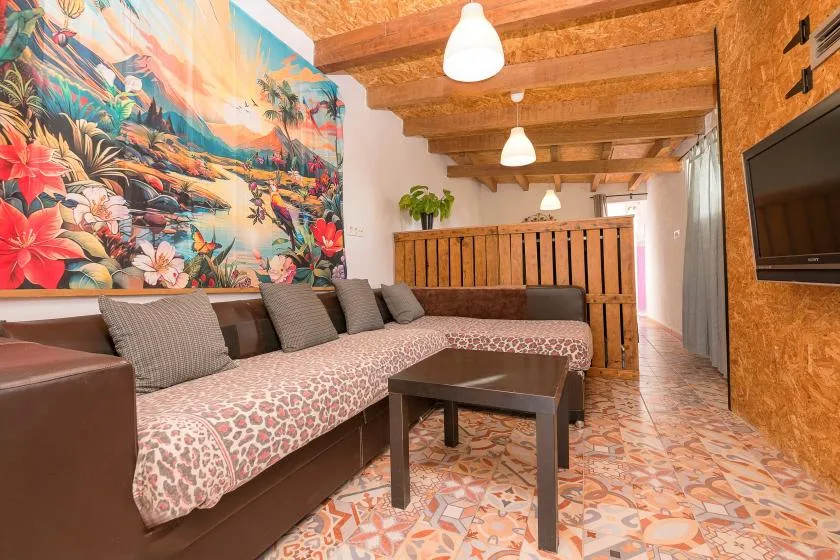 A lounge seating area with a colorful mural, wooden ceiling beams, and a small table.