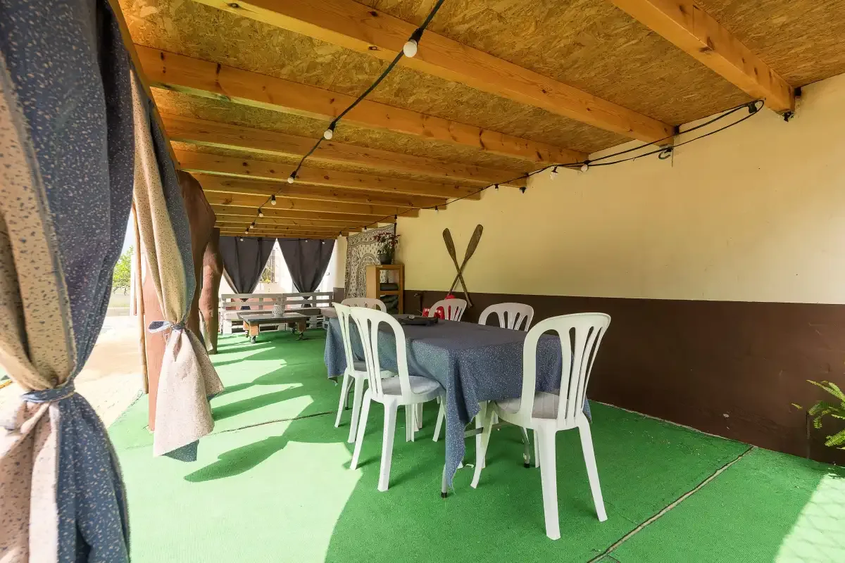 A covered outdoor dining area with tables and chairs on a green floor.