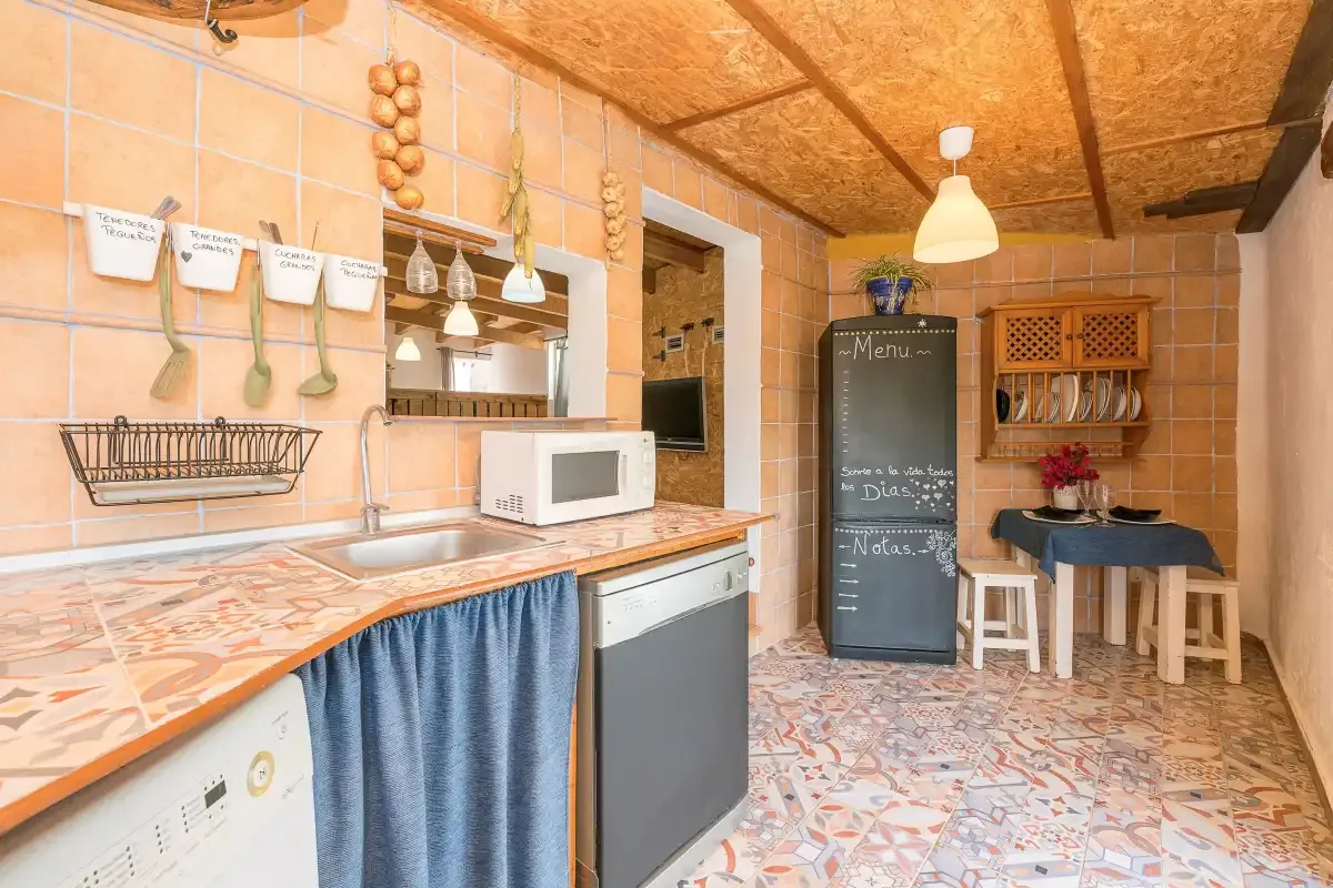 A tiled kitchen with a countertop, sink, microwave, and small dining table.