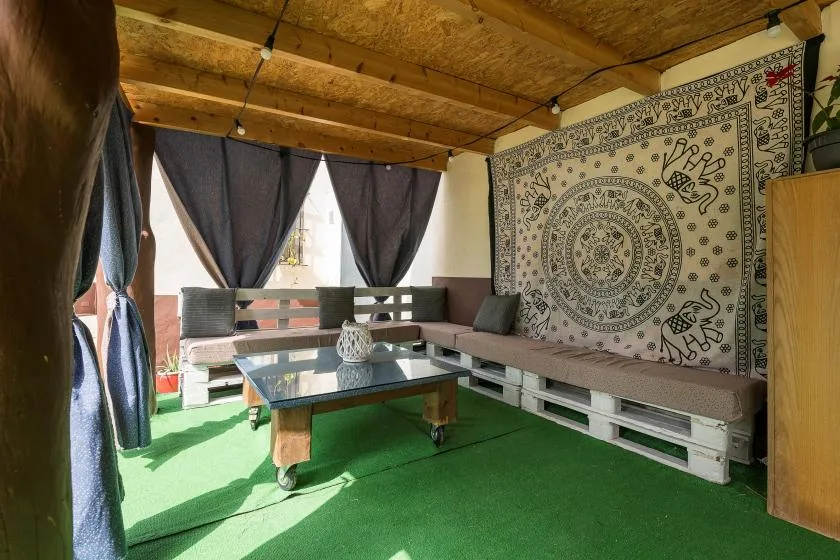 A covered lounge area with pallet seating, a low table, and a patterned wall hanging.