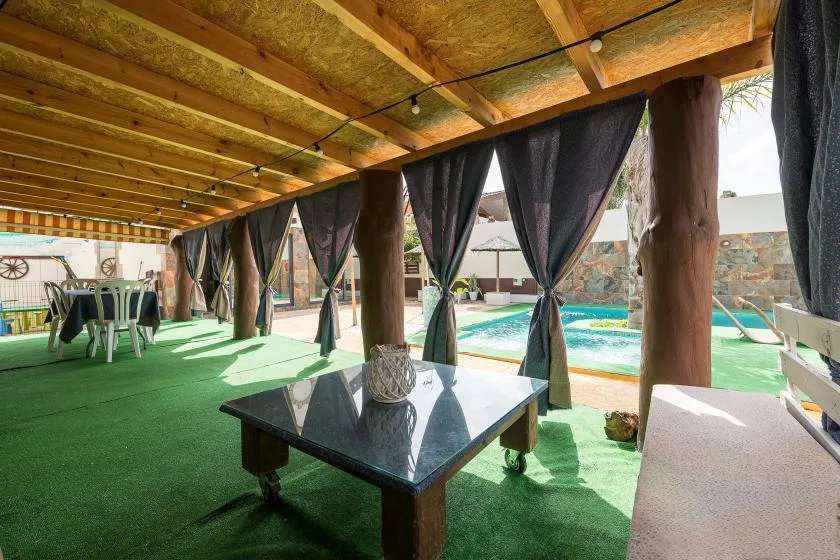 A shaded outdoor seating area with dark curtains overlooks a swimming pool.