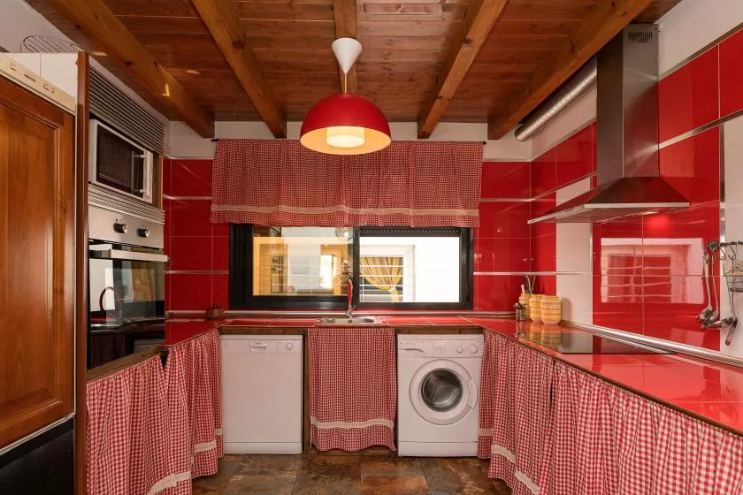 A red kitchen with wood ceiling beams and appliances along the counters.