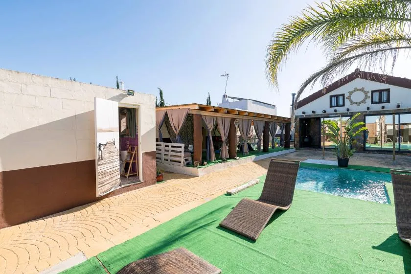 An outdoor pool area beside a covered patio, with lounge seating on the deck.