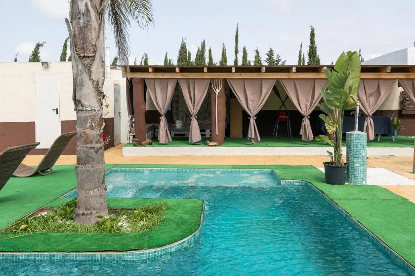 An outdoor swimming pool sits in front of a shaded patio with curtains.