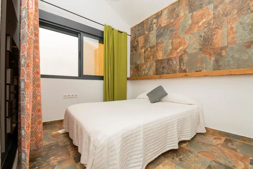 A bedroom with a bed, colorful stone-patterned wall, and window.