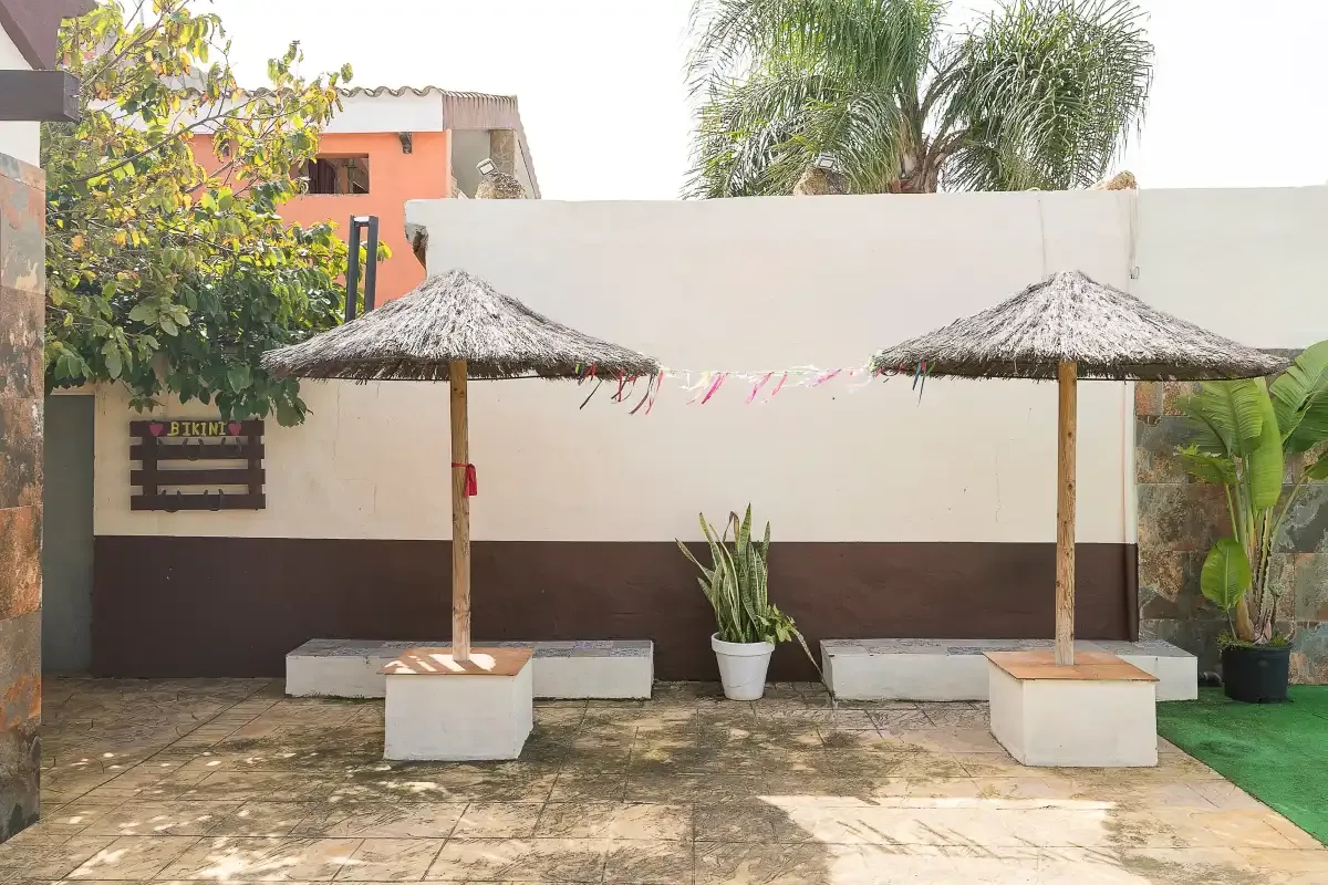 An outdoor patio has two thatched shade umbrellas and potted plants.